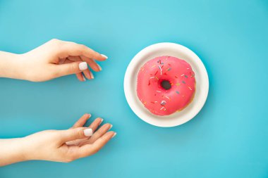 Female hands and donut on a blue background, flat lay, conceptual minimalism.