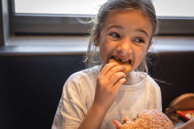 A little girl in a cafe eats fast food, a burger and fries.