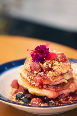 Appetizing pancakes decorated with berries and flowers close-up.