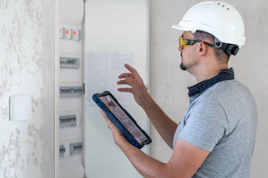 Elektrik santralinde fitillerle çalışan bir elektrik teknisyeni. Elektrik ekipmanlarının kurulumu ve bağlantısı.