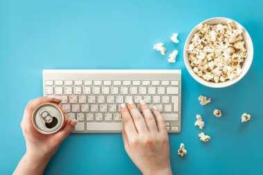Keyboard, female hands and popcorn on a blue background, the concept of watching movies, series, minimalism.