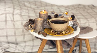 Cozy autumn composition with a cup of tea, candles and decorative details on a blurred background.