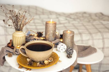 Cozy autumn composition with a cup of tea, candles and decorative details on a blurred background, copy space.