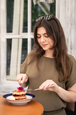 Attractive young woman in a cafe eating pancakes with berries on the terrace.