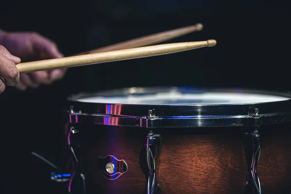 Drummer playing drum sticks on a snare drum on black background close up.