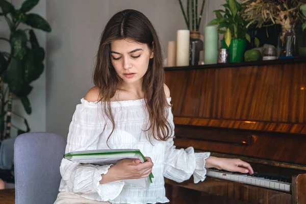 A beautiful young woman pianist looks at the notes and plays, sitting near the piano.