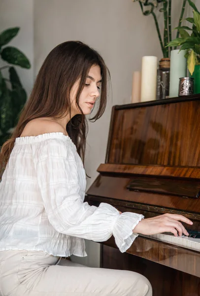 Beautiful young woman pianist plays the old wooden piano in the interior of the room.