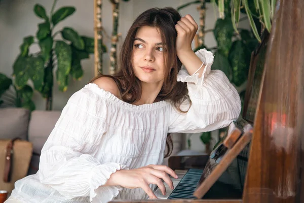 Beautiful young woman pianist plays the old wooden piano in the interior of the room.