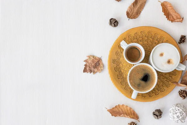 Autumn composition with cups of coffee and leaves on a textural white background, flat lay, copy space.