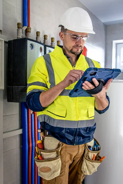 Man, an electrical technician in uniform working in a switchboard with fuses. Installation and connection of electrical equipment. Professional uses a tablet.