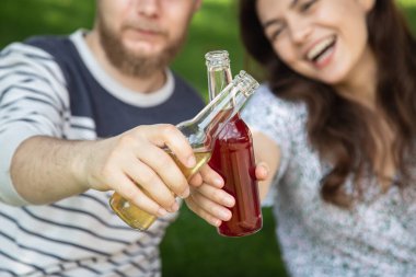 A young man and woman drinking drinks in glass bottles on a picnic, concept of summer drinks and outdoor recreation.