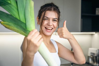 Mutfakta elinde pırasa olan neşeli genç bir kadın. Yemek pişirme ve sağlıklı beslenme kavramı..