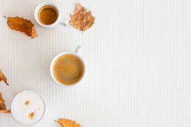 Autumn composition with cups of coffee and leaves on a textural white background, flat lay, copy space.