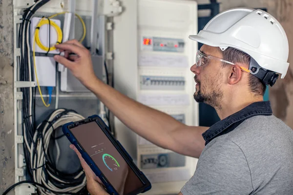 Man, an electrical technician working in a switchboard with fuses. Installation and connection of electrical equipment. Professional uses a tablet.