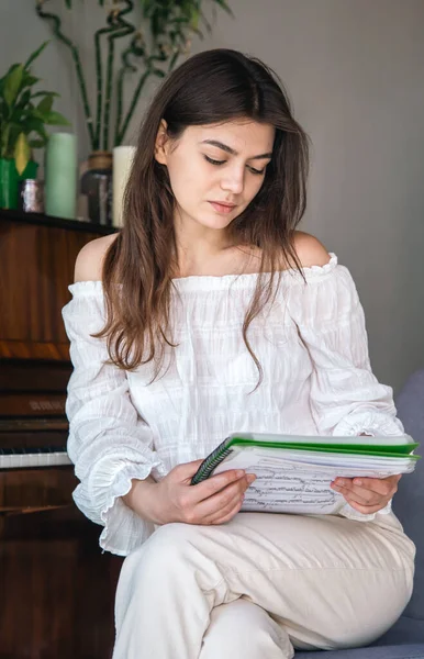 A beautiful young woman pianist looks at the notes while sitting near the piano.