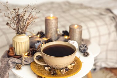 Cozy autumn composition with a cup of tea, candles and decorative details on a blurred background.
