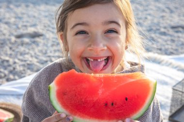 Close-up, funny little girl appetizingly eats watermelon on the sea beach.