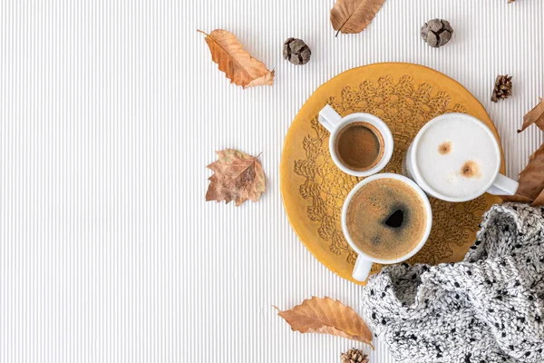 Autumn composition with cups of coffee and leaves on a textural white background, flat lay, copy space.