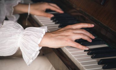 Female hands play on an old wooden piano, close-up.