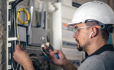 Elektrik santralinde fitillerle çalışan bir elektrik teknisyeni. Elektrik ekipmanlarının kurulumu ve bağlantısı.