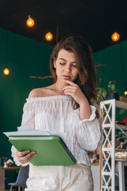 Beautiful business woman with a folder of papers in a green interior with light bulbs.