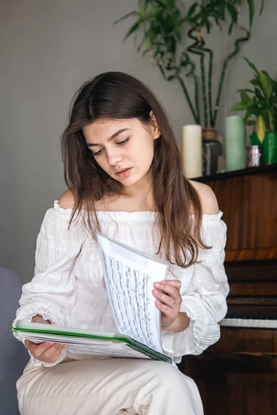 A beautiful young woman pianist looks at the notes while sitting near the piano.