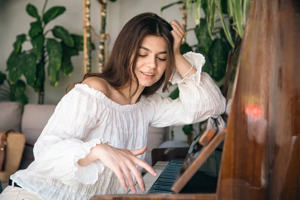 Beautiful young woman pianist plays the old wooden piano in the interior of the room.