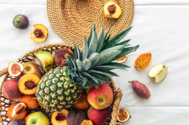 Beyaz arka planda sepette ananas ve diğer egzotik meyvelerle kompozisyon.