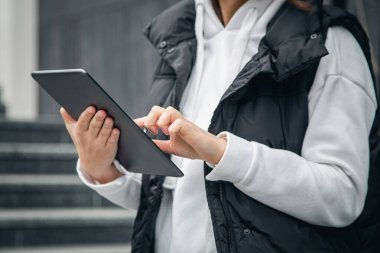 Yakın plan, bir kadın bulanık şehir arka planında, vücudun bir parçası olan bir tablet kullanır..