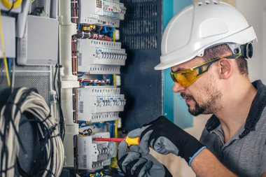 Elektrik santralinde fitillerle çalışan bir elektrik teknisyeni. Elektrik ekipmanlarının kurulumu ve bağlantısı.