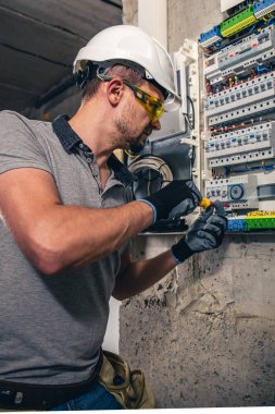 Elektrik santralinde fitillerle çalışan bir elektrik teknisyeni. Elektrik ekipmanlarının kurulumu ve bağlantısı. Profesyonel bir tablet kullanır.