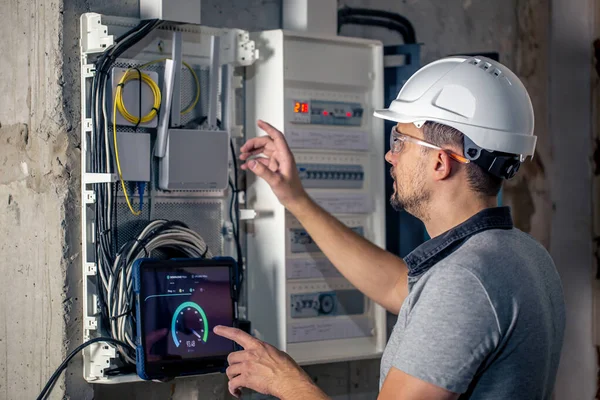 Man, an electrical technician working in a switchboard with fuses. Installation and connection of electrical equipment. Professional uses a tablet.