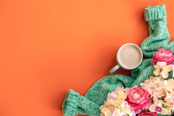 Spring orange background with a cup of coffee, flowers and a knitted element, flat lay, copy space.