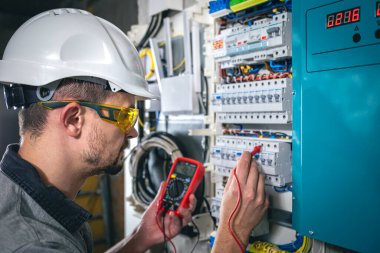 Elektrik santralinde fitillerle çalışan bir elektrik teknisyeni. Elektrik ekipmanlarının kurulumu ve bağlantısı. Profesyonel bir tablet kullanır.