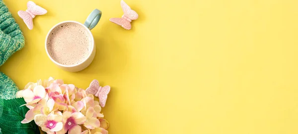Spring yellow background with a cup of coffee, flowers and a knitted element, flat lay, copy space.