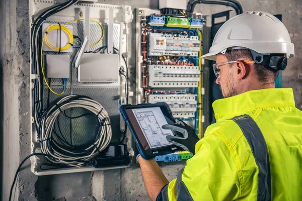 Man, an electrical technician working in a switchboard with fuses. Installation and connection of electrical equipment. Professional uses a tablet.