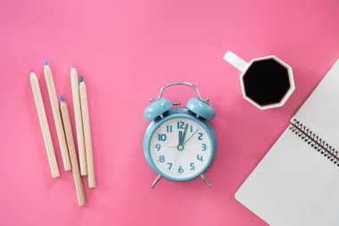 Pembe arka planda not defteri, çalar saat ve kahve fincanı olan düz bir yer, iş yeri konsepti..