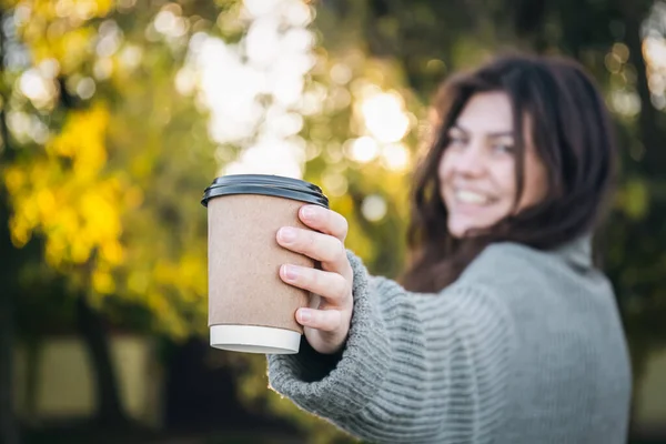 A young woman in a sweater with a cup of coffee in nature on a blurred background in the early autumn morning.