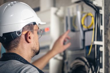 Elektrik santralinde fitillerle çalışan bir elektrik teknisyeni. Elektrik ekipmanlarının kurulumu ve bağlantısı.