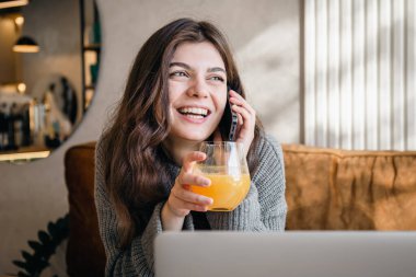 Çekici genç bir kadın telefonda konuşuyor ve sabahın erken saatlerinde dizüstü bilgisayarla çalışıyor..