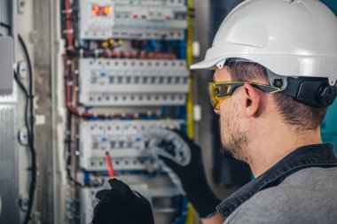 Elektrik santralinde fitillerle çalışan bir elektrik teknisyeni. Elektrik ekipmanlarının kurulumu ve bağlantısı.