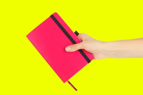黄色の背景に手にピンクのノートブック — ストック写真