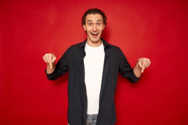Gülümseyen neşeli adam işaret parmağıyla bir şeyin reklamını yapıyor. Stüdyoda kırmızı arka planda duruyor, kameraya gülümsüyor. Reklam afişi, konsepte bak. panorama.