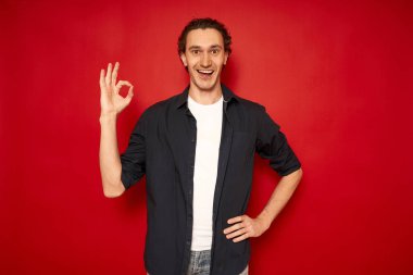 Gündelik giysiler içinde heyecanlı, mavi tişörtlü, beyaz tişörtlü genç yakışıklı adam, tamam işaretli kırmızı arka plan, mesaj, konsept - başarılı alışveriş, Noel indirimleri, promosyonlar