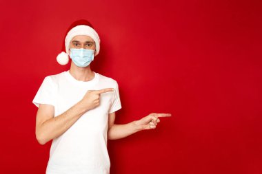 kavram - insanlar, sağlık, vücut dili, koronavirüs covid-19. Noel Baba 'nın Noel şapkalı maskeli adamı boş koltukta oturuyor. Reklam metni için alanı olan kırmızı stüdyo arka planında izole edilmiş.