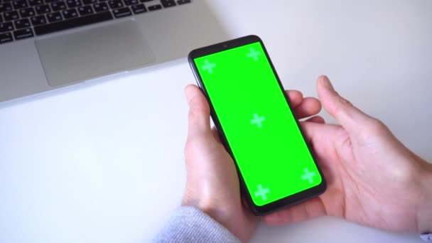 Κοντινό πλάνο. 4k. ένας άνθρωπος κρατά το smartphone με τα δύο χέρια, πιέζει το δάχτυλό του και παπύρους το κλειδί chroma της πράσινης οθόνης. κλικ στο εικονίδιο εφαρμογή, παίζει το παιχνίδι, σαρώνει με το δάχτυλό του, γράφει ένα μήνυμα — Αρχείο Βίντεο