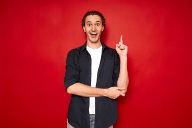 Ağzı açık heyecanlı bir adam işaret parmağını kaldırır, yeni parlak fikirle sevinir. Kırmızı arka planda izole edilmiş gündelik giysiler giyip mesaj atmak için. konsept - beyin fırtınası, bilgi, ilham