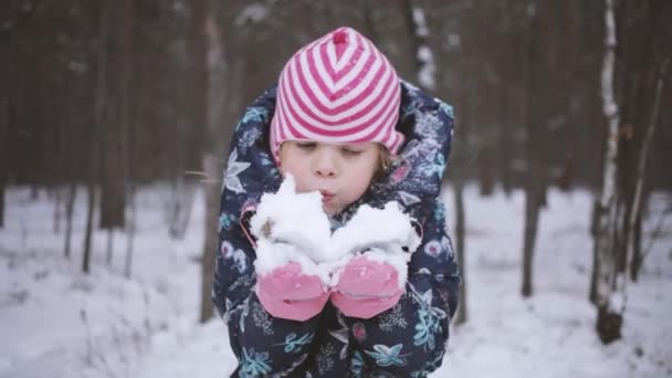 A menina segura um pedaço de neve em suas mãos e sopra nele. Crianças jogos antes do Natal — Vídeo de Stock