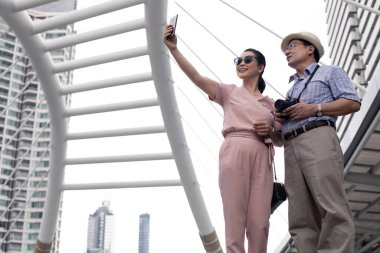 Kıdemli Asyalı çift, Tayland 'da tarihi bir gezideyken gün boyunca cep telefonlarının yanında selfie çekiyorlar. Yaşlı çift seyahat konsepti.