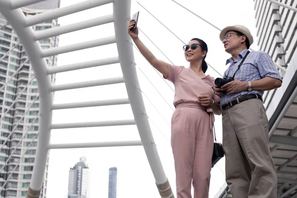 Kıdemli Asyalı çift, Tayland 'da tarihi bir gezideyken gün boyunca cep telefonlarının yanında selfie çekiyorlar. Yaşlı çift seyahat konsepti.